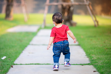 Toddler baby boy walking away along the path at the park.