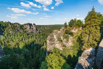 Bad Schandau in Bohemian Switzerland. Bastei bridge and mountain view. Narrow rock, natural sandstone arch in Europe..Hill scenery with greenery, blue sky and sunlight.