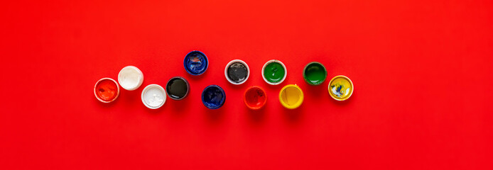 view from above of the colorful paints gouache in pots or cans on the colorful background wide long banner