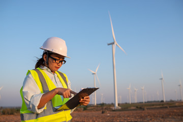 Fototapeta na wymiar women engineer working and holding the report at wind turbine farm Power Generator Station on mountain,Thailand people