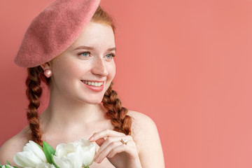 Happy smiling woman wearing pink beret, pearl earrings, ring, holding white tulips. Coral pink color background. Spring beauty, fashion concept. Copy, empty space for text