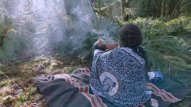 Woman shaman on a blanket burning plant medicine in a clay bowl talking with her ancestors