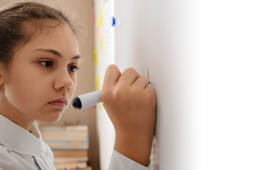 Concentrated female learner of secondary school writing some task on the whiteboard, thinking about the rules to write everything correctly