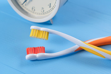 Two bright toothbrushes opposite each other with an analog alarm clock