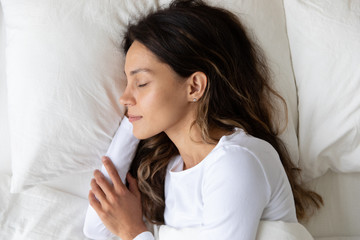 Top view of happy Caucasian millennial girl relaxing on soft white pillow sleep in cozy bed under...