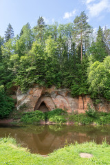 Sand stone cliffs and Salaca river. Red sandstones cave, water, trees and plants, green nature environment, climate concept..Angels cliff in Mazsalaca nature park, Latvia, Europe