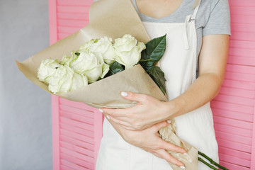 woman florist standing with bouquet of  white roses indoor in flower shop.  Small business, workplace concept
