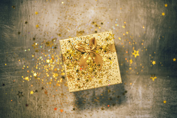 Christmas gift box with golden stars and sparkles on grey bacground. Gift box tied with golden...