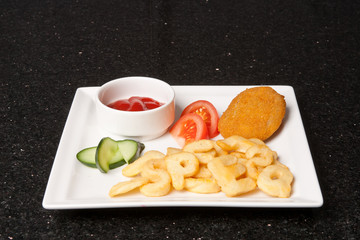 Alphabetic french fries, fried meat and ketchup, garnished with tomato and cucumber. Food concept on a white plate and black background