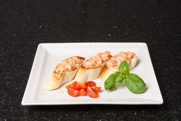 Savory Italian appetizers. Bruschetta with salmon and garnished with basil and tomato. Slices of toasted baguette and fish. Food concept on a white plate and black background
