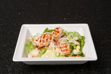 Green salad with chicken, cheese, croutons and apple. Food concept on a white plate and black background
