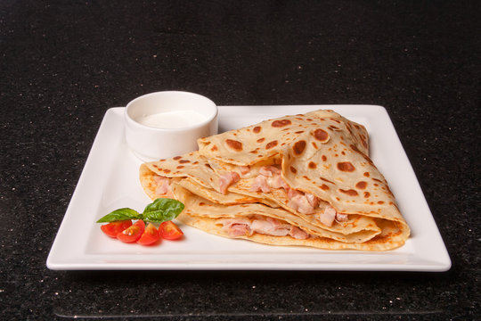 Pancake with ham, cheese and sour cream sauce. Food concept on a white plate and black background