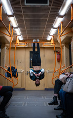 Girl hanging by feet upside down in the subway carriage and using smartphone. Concept of overusing social networks and addiction