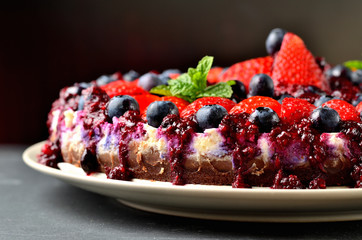 Cheesecake tart with fresh strawberries, blueberries and cherry jam. Dark background. Low depth of field