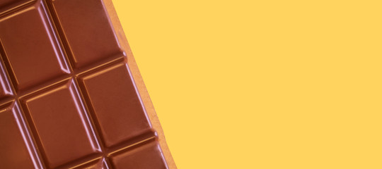 A bar of milk chocolate closeup on a yellow background. The concept of sweets, junk food. Detailed texture macro photo in warm colors. Banner.