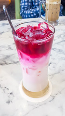 A pink and white drink beverage served in a long glass with a metal spoon in it. The drink is pink on the top and white on the bottom. There is a lot of ice cubes in it. Refreshing beverage.