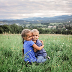 Cute 7-8 years girl hugging her smaller on the top of the mountains in summer