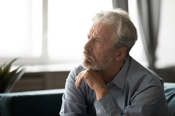 Pensive depressed elderly male look in distance thinking pondering at home, thoughtful unhappy mature man lost in thoughts feel lonely abandoned, mourn or yearn, old people solitude concept