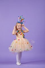 Childrens birthday party, masquerade. Little happy toddler child girl in a puffy tutu fancy dress, having fun on Violet background. Space for text