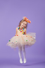 Childrens birthday party, masquerade. Little happy toddler child girl in a puffy tutu fancy dress, having fun on Violet background. Space for text