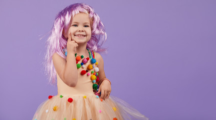 Childrens birthday party, masquerade. Little happy toddler child girl in a puffy tutu fancy dress, having fun on Violet background. Space for text