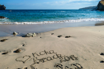 Idyllic beach with 'Koka Beach' sign on the sand, Flores, Indonesia. The waves are gently washing the shore. There are some rocks popping out from the sea water. Serenity and calmness. Turquoise sea.