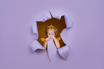 Cute little child girl in princess costume breaks through a colored purple paper wall. Points with...