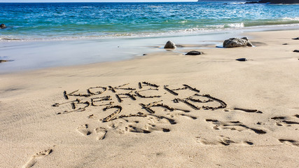 Idyllic beach with 'Koka Beach' sign on the sand, Flores, Indonesia. The waves are gently washing the shore. There are some rocks popping out from the sea water. Serenity and calmness. Turquoise sea.