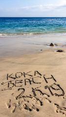 Idyllic beach with 'Koka Beach' sign on the sand, Flores, Indonesia. The waves are gently washing the shore. There are some rocks popping out from the sea water. Serenity and calmness. Turquoise sea.