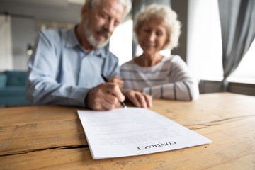 Close up of happy mature 60s couple spouses clients close deal sign insurance contract with...