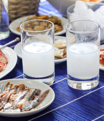 Ouzo, raki alcohol with ice cubes next to seafood meze