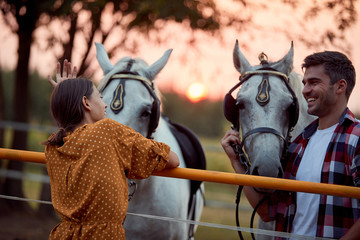 Smiling couple on the ranch at sunset preparing their horses for a ride