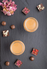 Sweet chocolate liqueur in glass with chocolate candies on a black stone slate board. Top view, copy space.