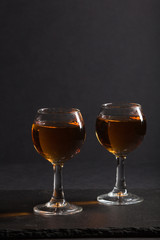 Glass of whiskey on a black stone slate board on black background. Side view, low key, copy space.