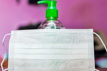 Disposable paper mask placed infront of a bottle of hand sanitizer.