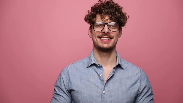 attractive casual man wearing glasses standing and smiling happy then yelling and then turning his head to aside on pink studio background