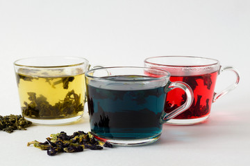 butterflu pea blue hot tea. Three glass cups with blue, red and green tea with dry tea leaves and flowers on a white background. Red hot Hibiscus tea. Green hot tea. Hot drinks. Healthy lifestyle.
