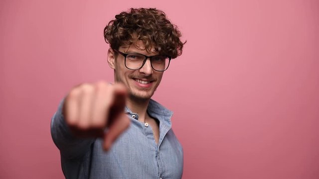handsome casual man wearing glasses standing and looking at camera happy while pointing forward confident on pink studio background