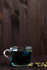 Obraz na płótnie Canvas butterflu pea tea. Healthy lifestyle. glass of hot blue tea with dry flowers on a black background. blue herbal tea on a wooden background. Fresh Cold drinks. copy space