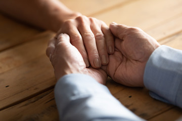 Crop close up of supportive old mature 60s man hold caress comfort middle-aged woman hands sitting...