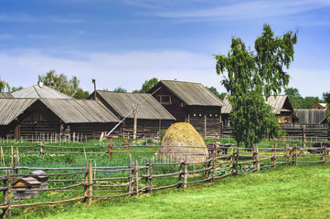 Old wooden log hut in a russian villageduring a sunny summer time. Traditional rural landscape in Russia, haystack, beehives, izba, green grass and blue sky.