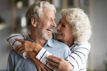 Happy elderly retired 60s husband and wife hug cuddle look in eyes share close tender moment...