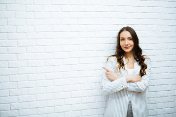 smiling business woman showing teeth at work with long dark hair in white jacket with her hands on her belly and pointing to the right hand with a finger draws on a white wall © ostap_davydiak