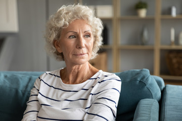 Fototapeta na wymiar Pensive old middle-aged 60s woman look in distance thinking pondering, thoughtful elderly lady sit relax on couch in living room daydreaming or visualizing, lost in thoughts missing mourning