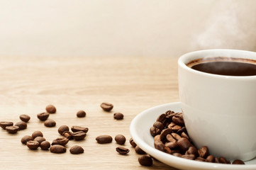 Coffee cup with hot steam and coffee beans on a wooden table with space background