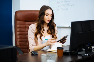 beautiful young business woman boss dark-haired boss with long wavy healthy hair sitting at workplace on big office chair