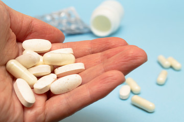 A pile of white pills in a female hand on a background of scattered pills.