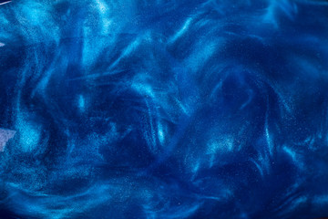 The texture of a shiny glitter blue drink, with sparkles streaks across the surface of the water....