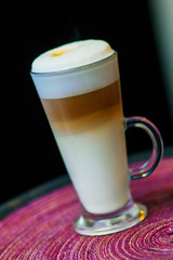 Delicious layered cappuccino or latte macchiato coffee served in a long glass. Cup of coffee in clear long glass on a tray.