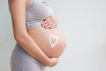 Pregnant woman holding red heart and hand on her belly, symbol of new life, concept of expecting for baby and extending family